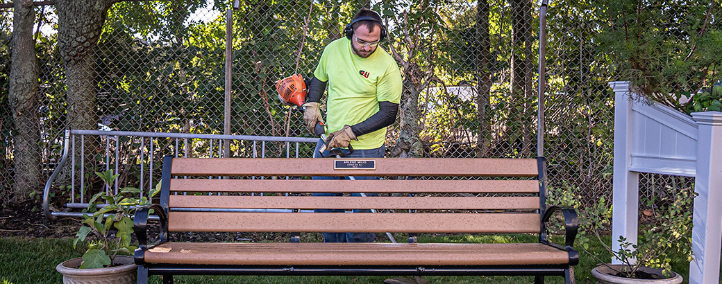Person using a weed whacker to tidy behind a park bench
