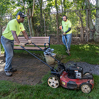 Two people performing lawn maintenance around a park bench