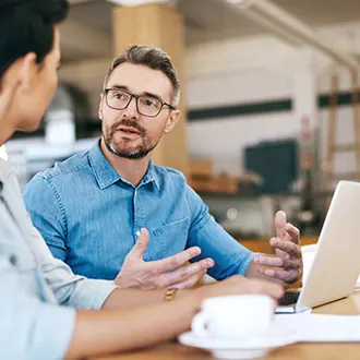 Two people in a meeting, one has a laptop open in front of them