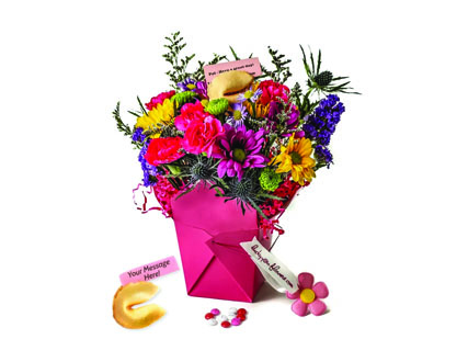 Bouquet of flowers arranged in a pink box reminiscent of a Chinese food takeout container. A fortune cookie is rested beside it.