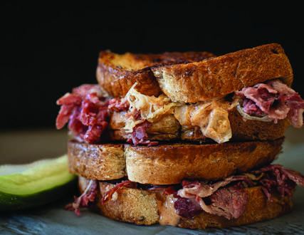 Two grilled sandwiches stacked on top of each other, filled with meats and melted cheese